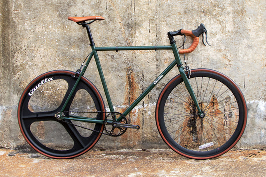 Green bicycle with brown handlebars and tires against a textured wall.