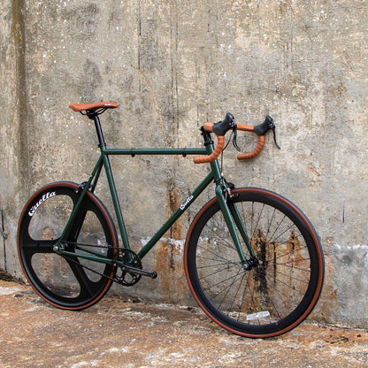 Green bicycle with brown handlebars and seat against a textured wall.
