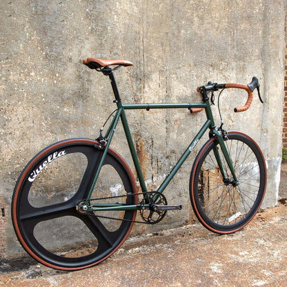 Green bicycle with black and black wheels against a textured wall.