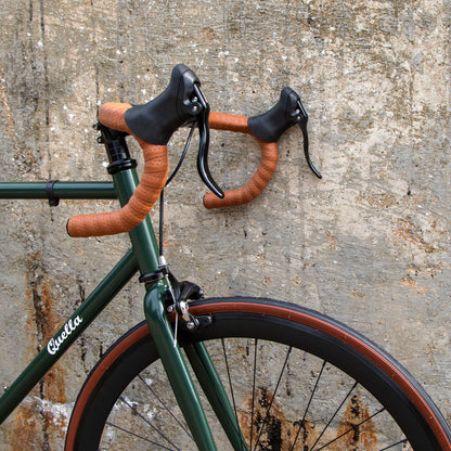 Green bicycle with brown handlebars against a textured wall