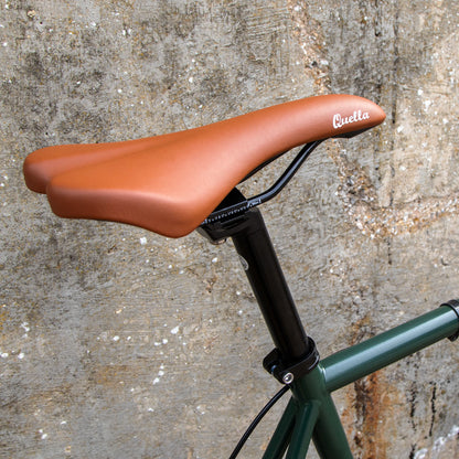 Brown bicycle seat with 'Quella' branding against a textured wall background